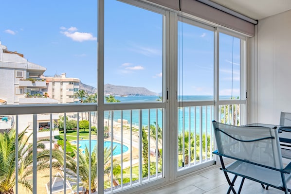 A balcony with a view of a swimming pool, palm trees, and a distant mountain.