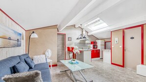 A modern kitchen with red cabinets, a dining area with a glass table, and a living room with a blue sofa. - Le Grand T2 – Stylish Apartment with Shared Pool in Andernos-les-Bains (Andernos-les-Bains)