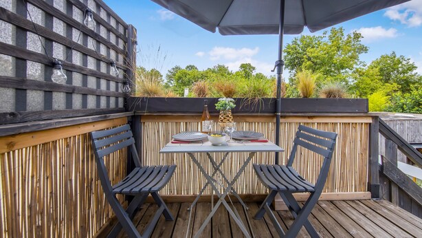 An outdoor patio with a table set for two, surrounded by wooden chairs, under a large umbrella. - Le Grand T2 – Stylish Apartment with Shared Pool in Andernos-les-Bains (Andernos-les-Bains)
