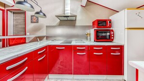 A modern kitchen with red cabinets, a stainless steel range hood, a double oven, and a refrigerator. - Le Grand T2 – Stylish Apartment with Shared Pool in Andernos-les-Bains (Andernos-les-Bains)