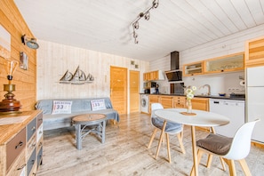 A cozy cabin interior with a wooden floor, a sofa, a dining table, and a kitchen area.