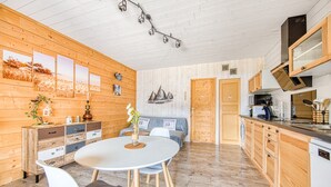 A modern kitchen with wooden cabinets, a dining area with a round table, and a built-in oven. - La Gascogne in Andernos-les-Bains – Stylish Apartment for 2, Near Nature & Coast (Andernos-les-Bains)