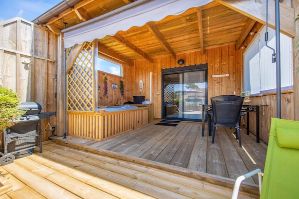 A wooden deck with a grill, a covered seating area, and a door leading to an indoor space.