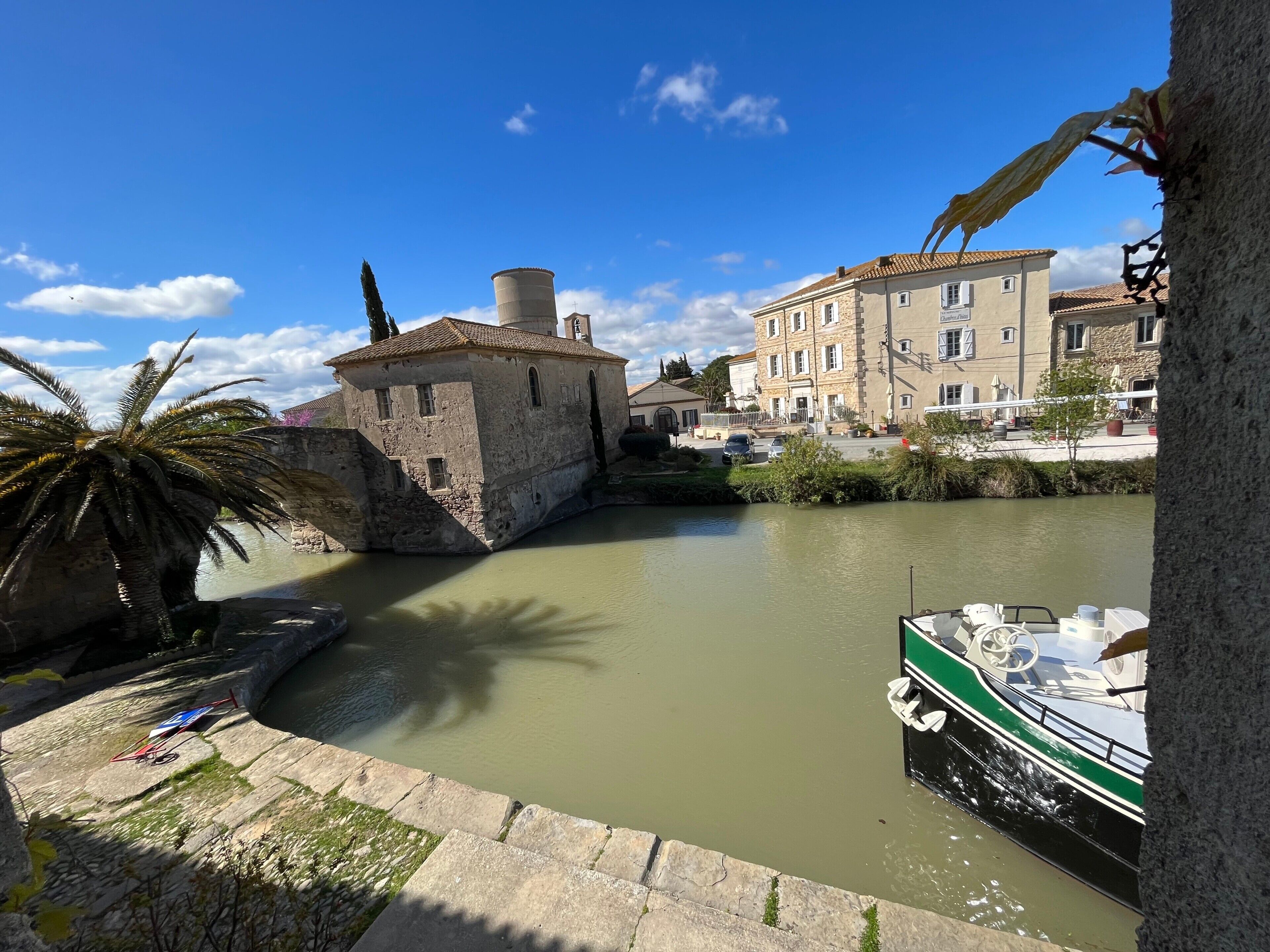 Un edificio storico con facciata in pietra, una palma e una barca ormeggiata sull'acqua.