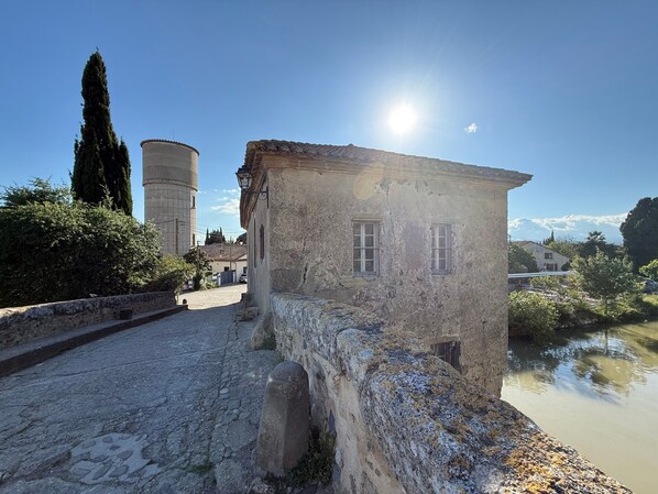 A stone building with two windows, a stone wall, and a cobblestone path.