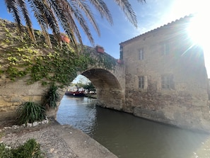 A stone bridge over a canal with a boat, surrounded by greenery and historic buildings.
