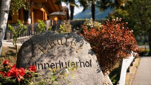 A stone monument with carved text, surrounded by greenery and a building in the background. - Chalet Palme: Mediterranean Garden & Terrace, Pool & Hot Tub for All Guests (Rifiano)