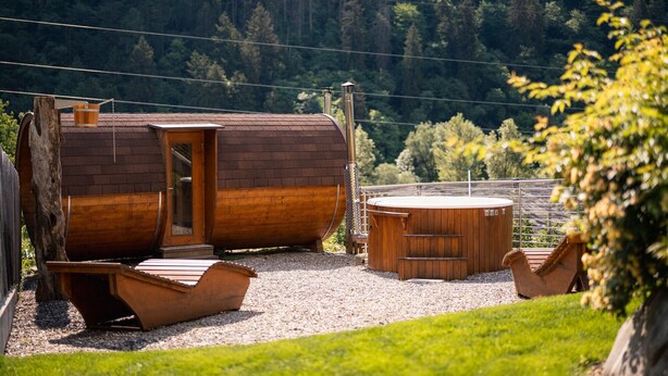 A wooden cabin with a door, a hot tub, and a wooden boat on a gravel path. - Chalet Palme: Mediterranean Garden & Terrace, Pool & Hot Tub for All Guests (Rifiano)