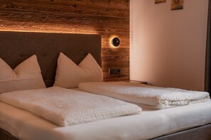 Un lit avec une tête de lit en bois, deux oreillers et une table de chevet dotée d’une lampe fixée au mur.