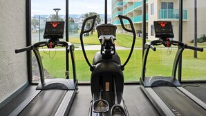 Three stationary bikes with digital displays, a window with a view of a building and a lawn.