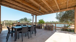 Un patio exterior con techo de madera, una mesa con sillas y vistas a una piscina.