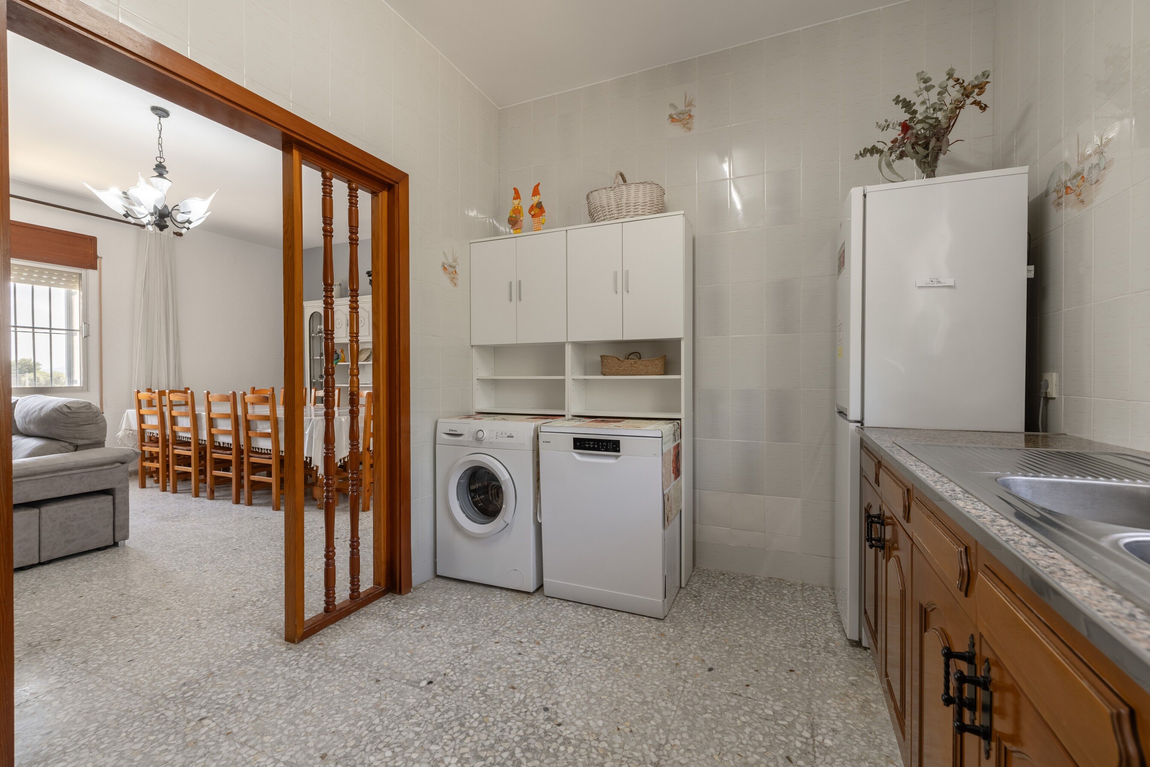 A kitchen with a washing machine, a refrigerator, and a dining area with chairs and a table.