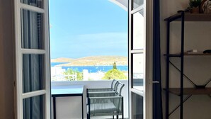 Un balcon ouvert avec une chaise, une vue sur la mer et une étagère avec quelques objets.