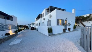 Une maison moderne à deux étages, avec une allée en gravier, des murs extérieurs blancs et une voiture garée dans l’allée.