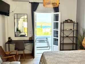 A bedroom with a bed, a desk, a chair, a mirror, a shelf, and a view of the outdoors.