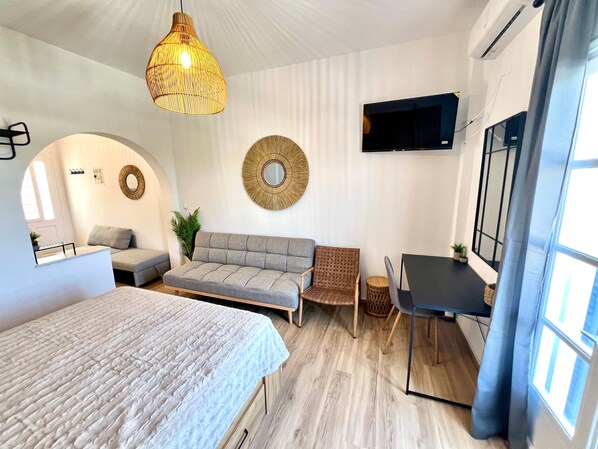 A modern room with a bed, sofa, desk, and TV.