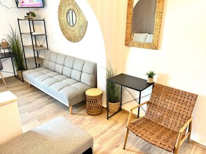 Una sala de estar moderna con un sofá, una mesa redonda, una silla de mimbre, una mesita auxiliar y un espejo fijado a la pared.