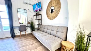 En moderne stue med sofa, fjernsyn, et rundt spejl og et lille bord.