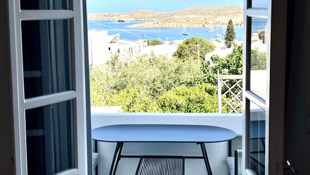 En balkon med et bord og stole, med udsigt over et vandareal med både og bygninger i det fjerne.