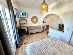 Una habitación moderna con cama, sofá, televisor y zona de cocina.