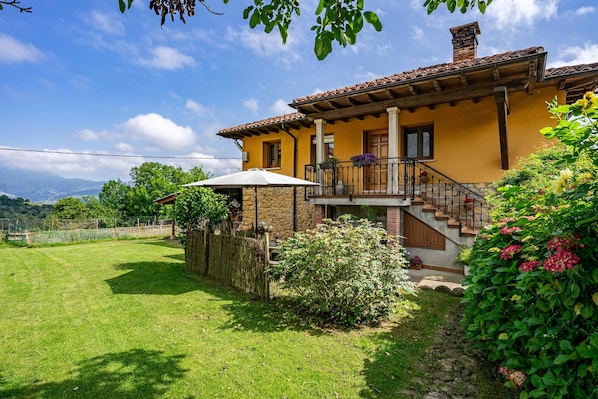 A yellow house with a stone facade, a wooden staircase, and a balcony with potted plants.