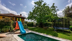A swimming pool with a slide, a trampoline, and a house in the background.