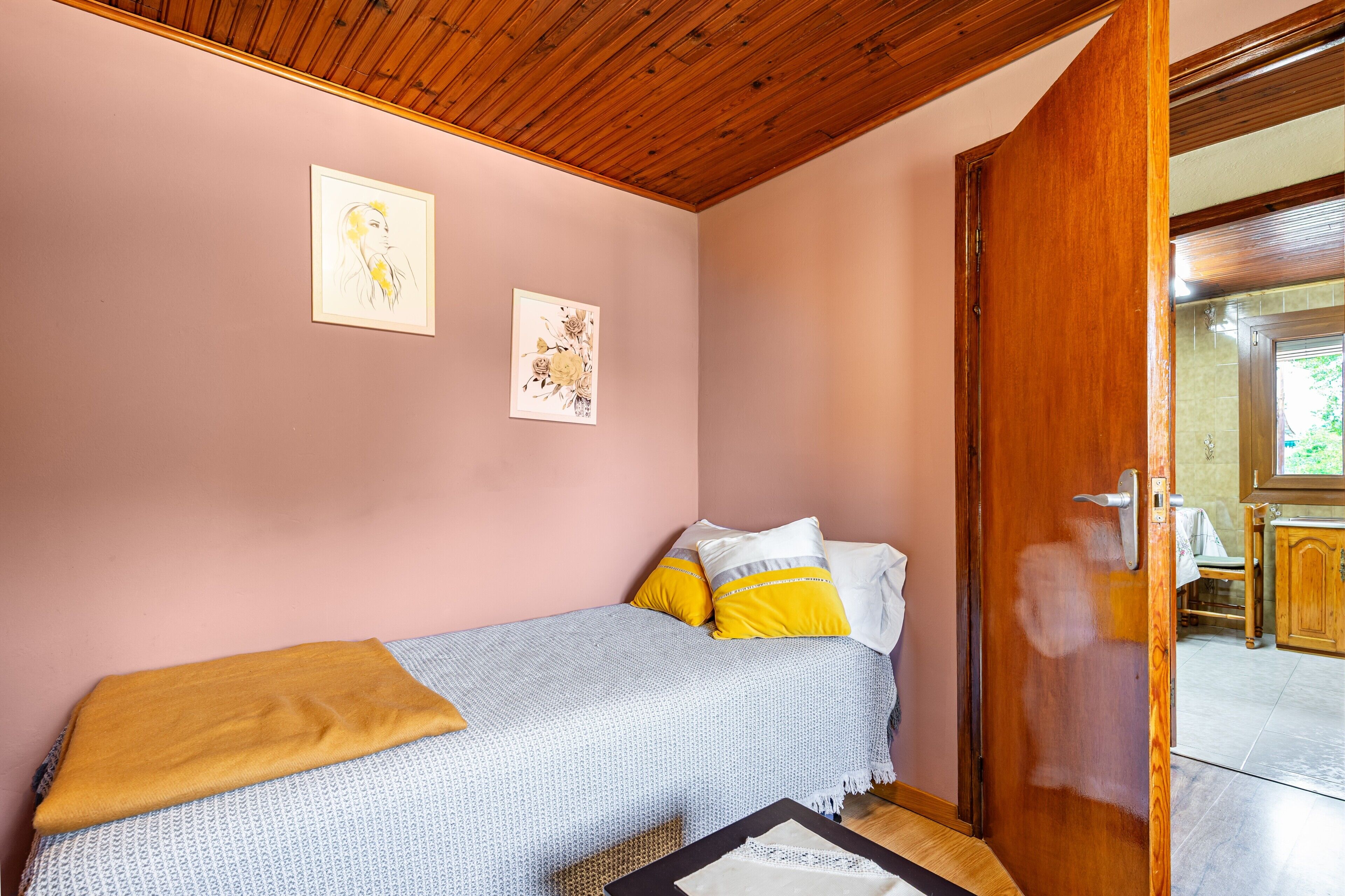 A bedroom with a bed, a wooden door, and a view of a kitchen area.