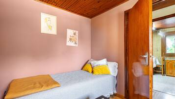 A bedroom with a bed, a wooden door, and a view of a kitchen area.