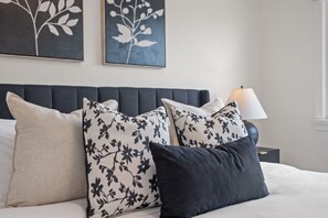 A neatly made bed with a dark headboard, two floral-patterned pillows, and a plain pillow. - Upscale Toronto Home Near Transit | Office | King Beds | Garden | Backyard Oasis (Toronto)
