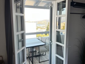 Een open balkon met een tafel en stoelen, uitzicht op een waterpartij en een gebouw in de verte.