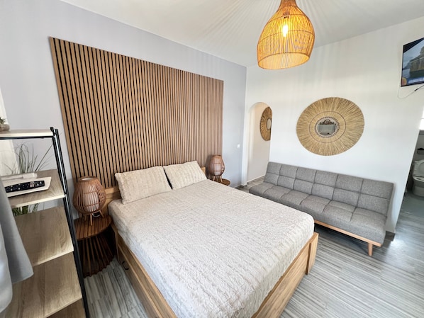 A modern bedroom with a bed, a sofa, a wall-mounted TV, and a unique wooden headboard.