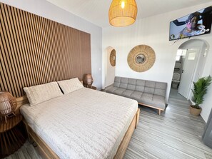 Un dormitorio moderno con cama, sofá, televisor y un espejo circular en la pared.