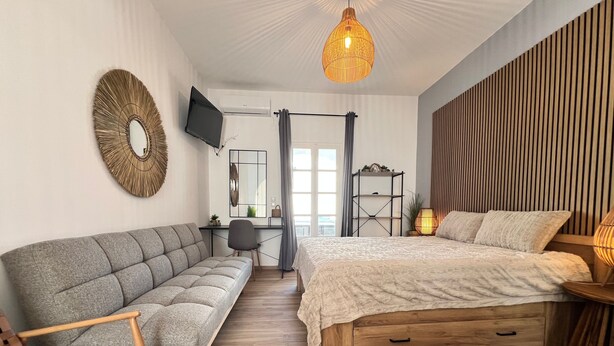 A bedroom with a sofa, a bed, a desk, a TV, and a hanging light fixture.