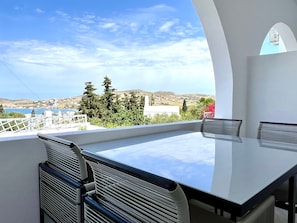 A terrace with a table and chairs, overlooking a scenic landscape with hills and a body of water.