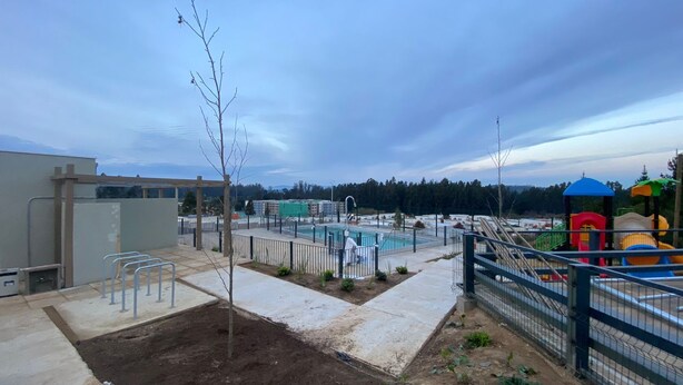 Zona de piscina con terraza cercada, un pequeño jardín y un parque infantil con estructuras de juego coloridas.
