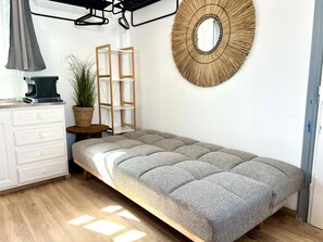 Une pièce bien rangée, avec un canapé gris recouvert de tissu, une table d’appoint en bois ornée d’une plante, une commode blanche et un miroir fixé au mur.