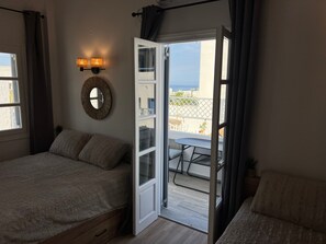 Une chambre à coucher comprenant un lit, une table de chevet, un miroir et une porte donnant sur un balcon équipé d’une table et de chaises.