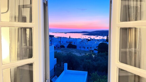 A view through a window with a clear sky, a body of water, and buildings in the distance.