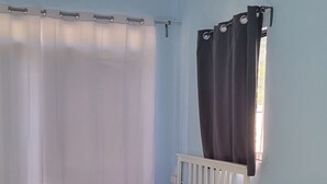 Una habitación con cama, mesa, silla, ventilador de techo y ventana con cortinas.