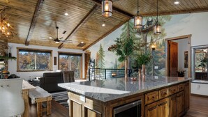 A spacious kitchen with a large island, wooden cabinetry, and a mural of a forest scene. - Shem Shack (Big Bear City)