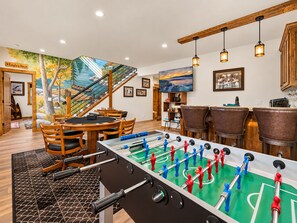 A room with a foosball table, wooden chairs, a dining table, and a mural on the wall. - Shem Shack (Big Bear City)