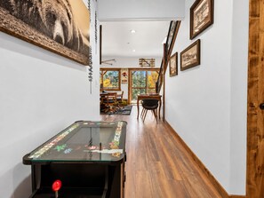 A narrow hallway with a pool table, wooden flooring, and framed pictures on the walls. - Shem Shack (Big Bear City)