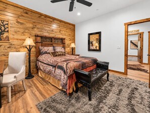 A bedroom with a wooden headboard, a bed with patterned bedding, a chair, a floor lamp, and a rug. - Shem Shack (Big Bear City)