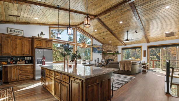 A spacious kitchen with wooden cabinets, a large island, and a dining area with a sofa and table. - Shem Shack (Big Bear City)