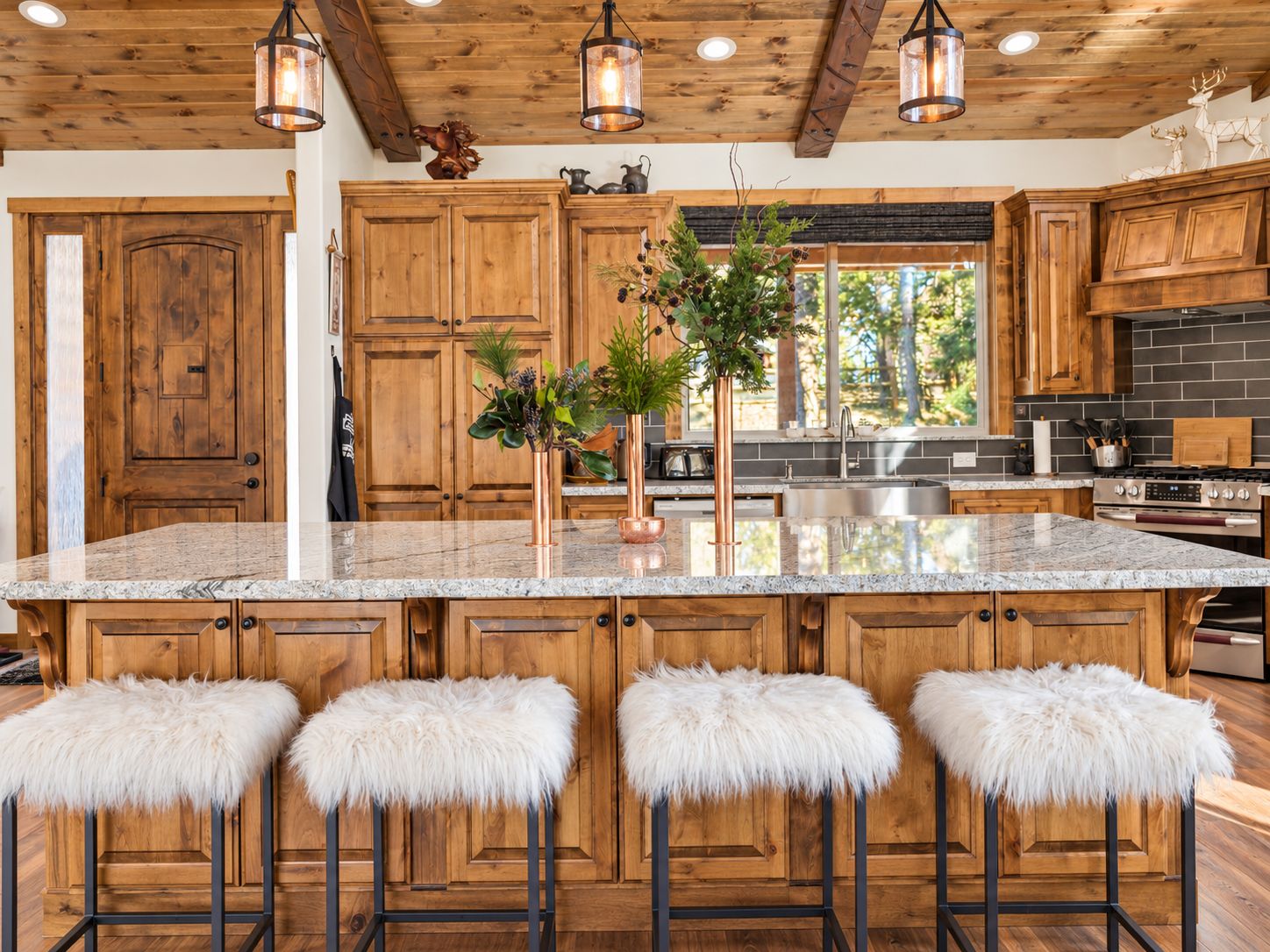 A spacious kitchen with wooden cabinets, a large island with stools, and pendant lighting.