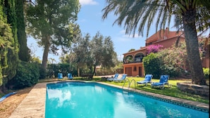 A swimming pool with lounge chairs, surrounded by trees and a building with a balcony. - Los Caños, Mediterranean Villa, bbq, pool, 5min-beach (Jávea)