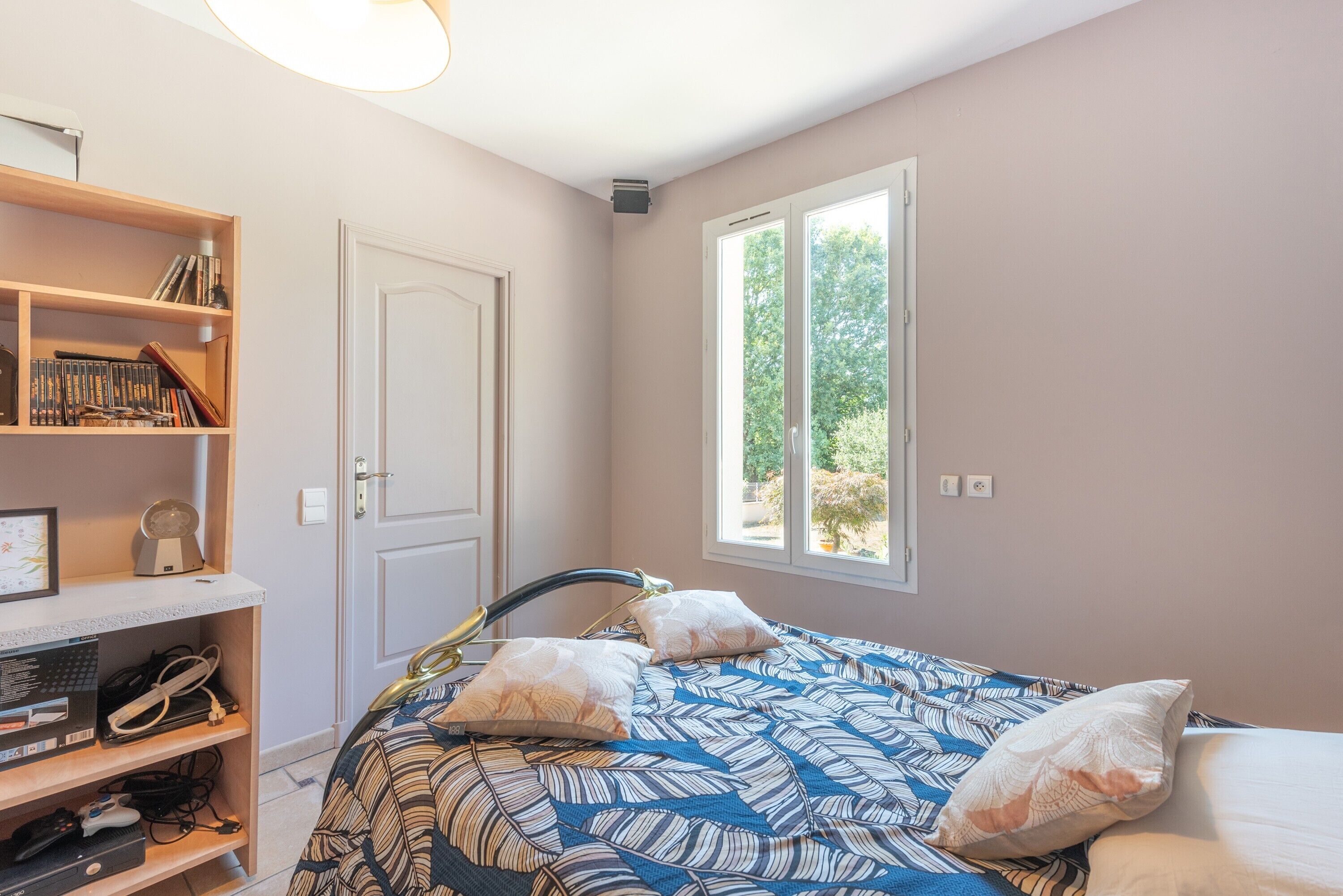 A bedroom with a bed, a bookshelf, a door, and a window.