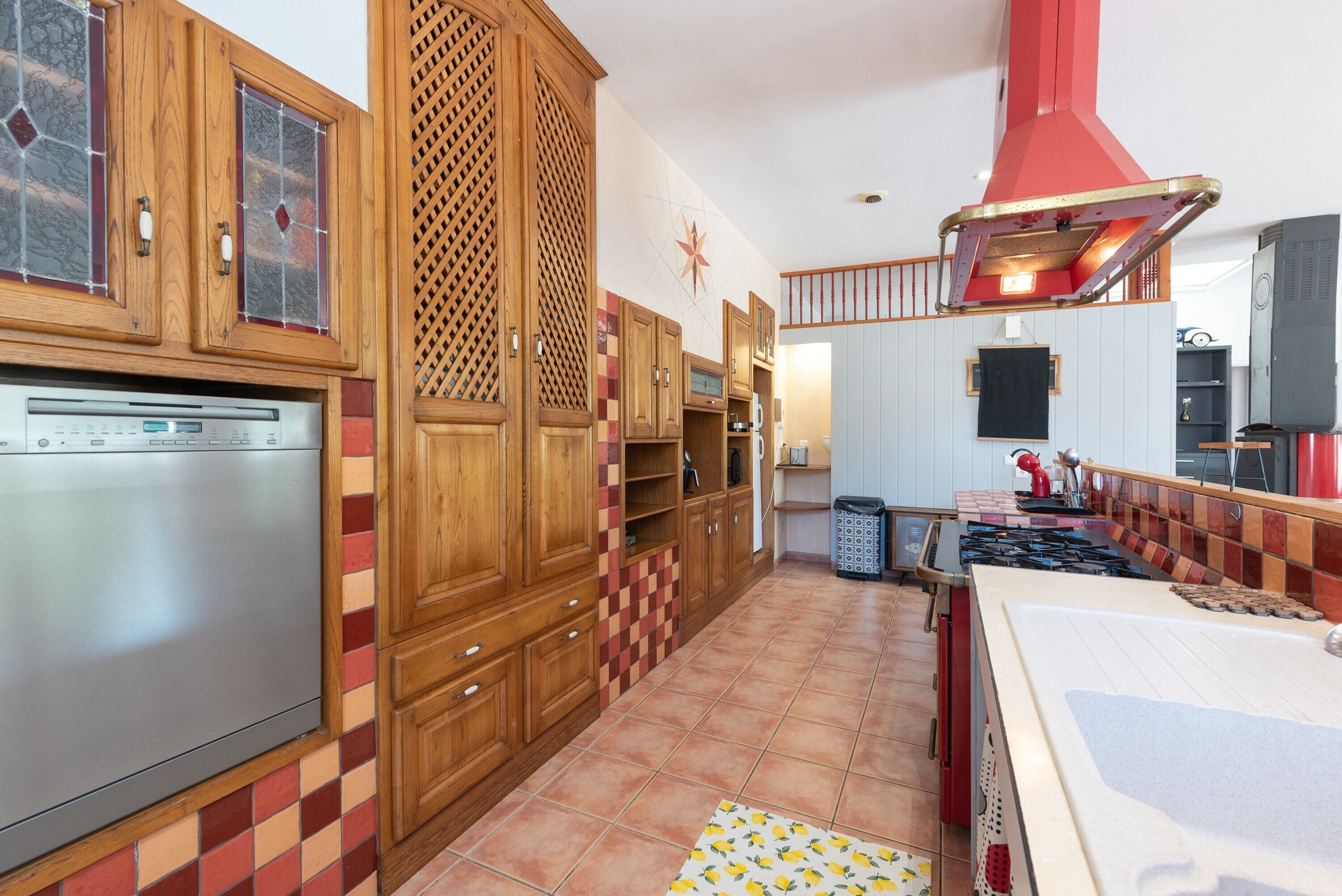 Eine Küche mit Holzschränken, einem Edelstahl-Kühlschrank, einer gefliesten Spritzschutzwand und einer roten Dunstabzugshaube.