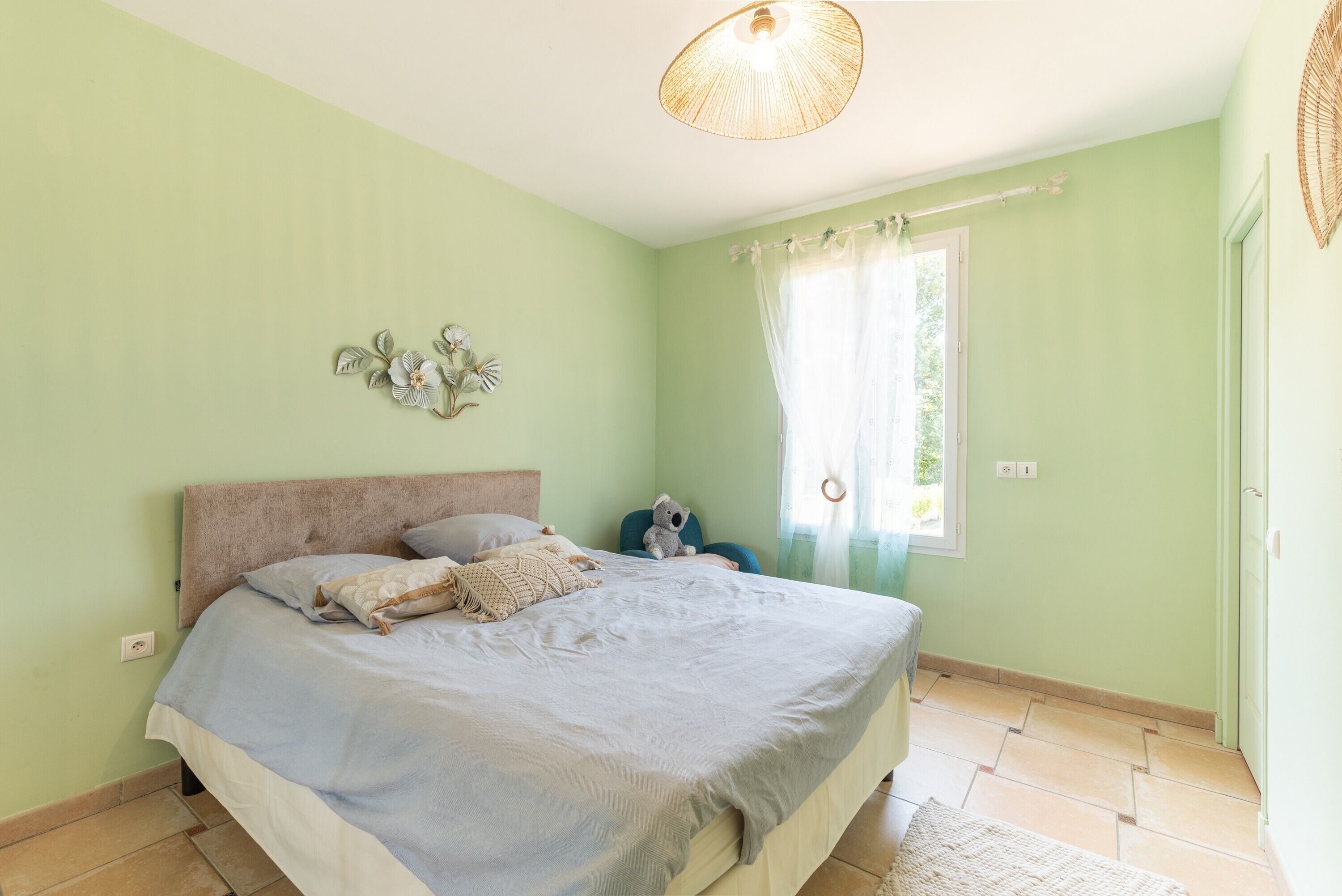 Ein Schlafzimmer mit einem Bett, einem Fenster mit Vorhängen, einer Wanddekoration und einer Deckenleuchte.