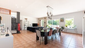 A spacious living area with a dining table, chairs, a TV, and a kitchen area with a stove. - Holiday Home 'Maison Zoé' with Private Pool, Private Terrace and Wi-Fi (Saint-Laurent-de-Neste)